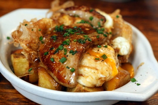 A bowl of fried potato chunks topped with runny fried eggs, foie gras, and chives.