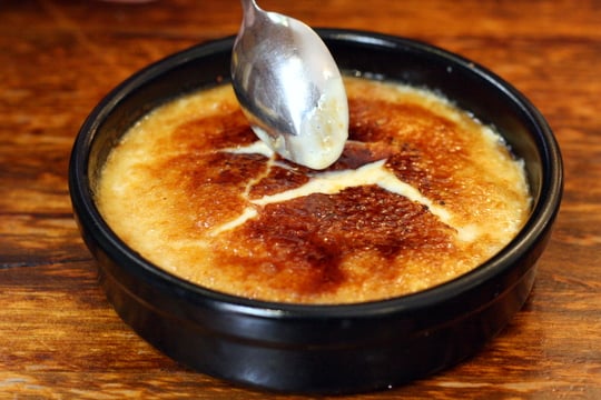 A bowl of crema catalana with a caramelized sugar top being broken by a spoon.