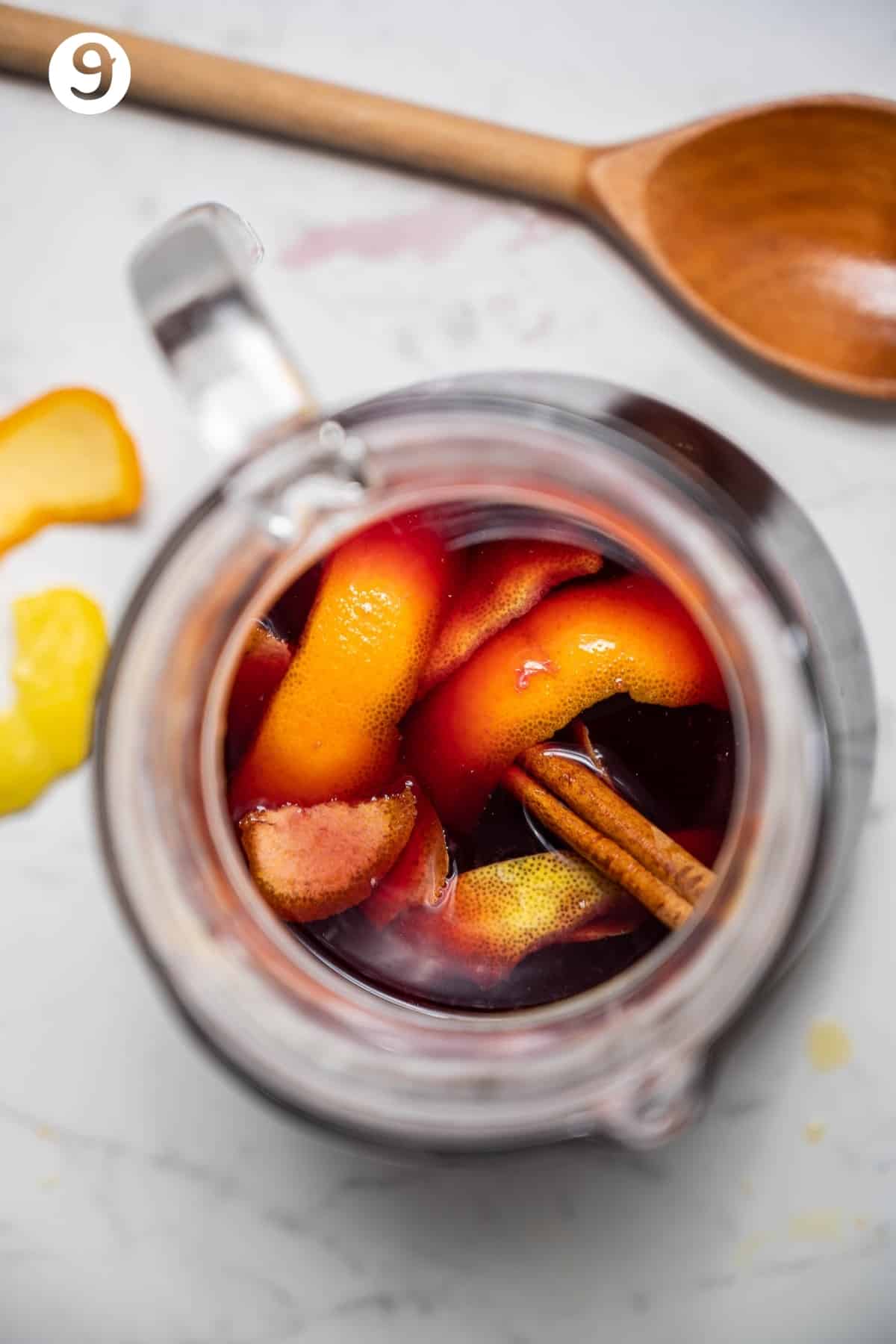 Overhead shot of a pitcher of red sangria with cinnamon stick, citrus peels, apple and nectarine.