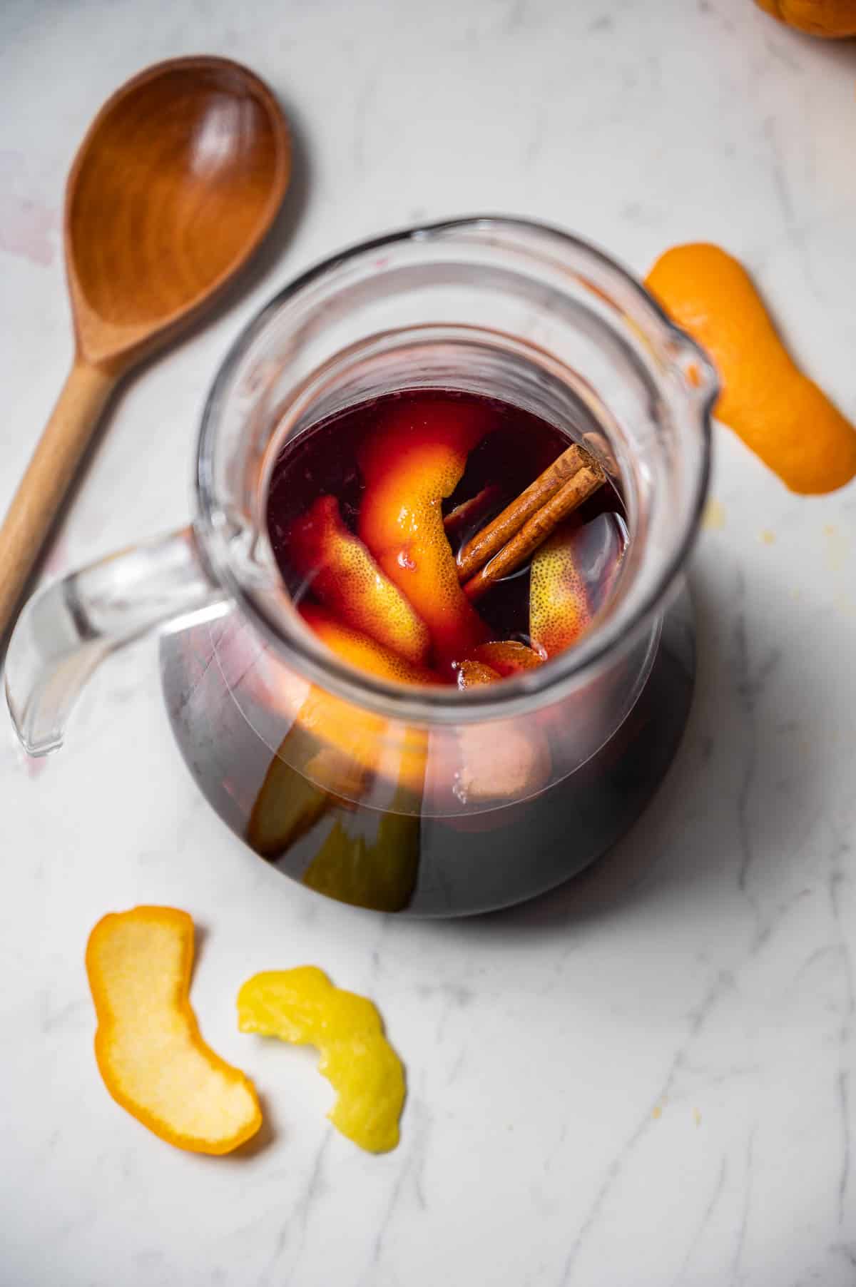 Pitcher of classic red sangria with citrus peel and cinnamon stick. A wooden spoon next to it.