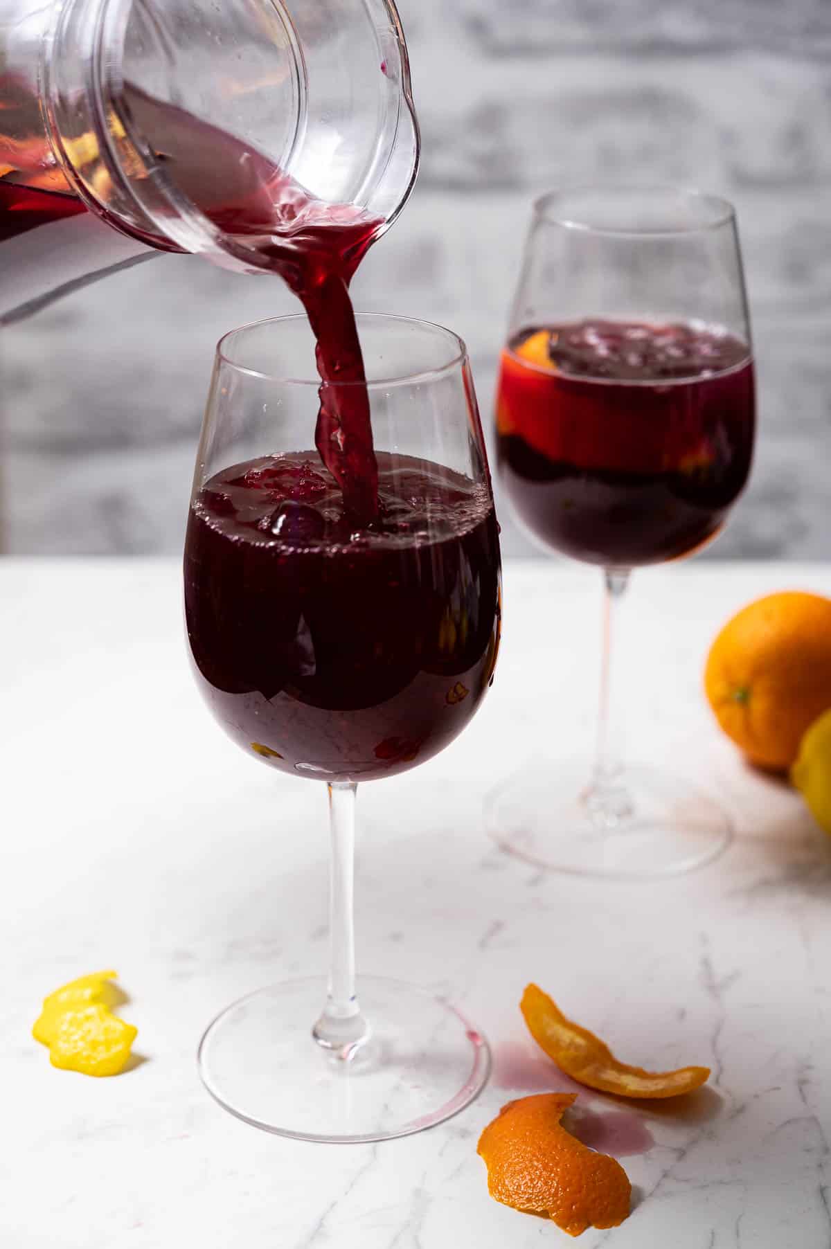 Pouring a glass of sangria out of a clear pitcher on a white countertop