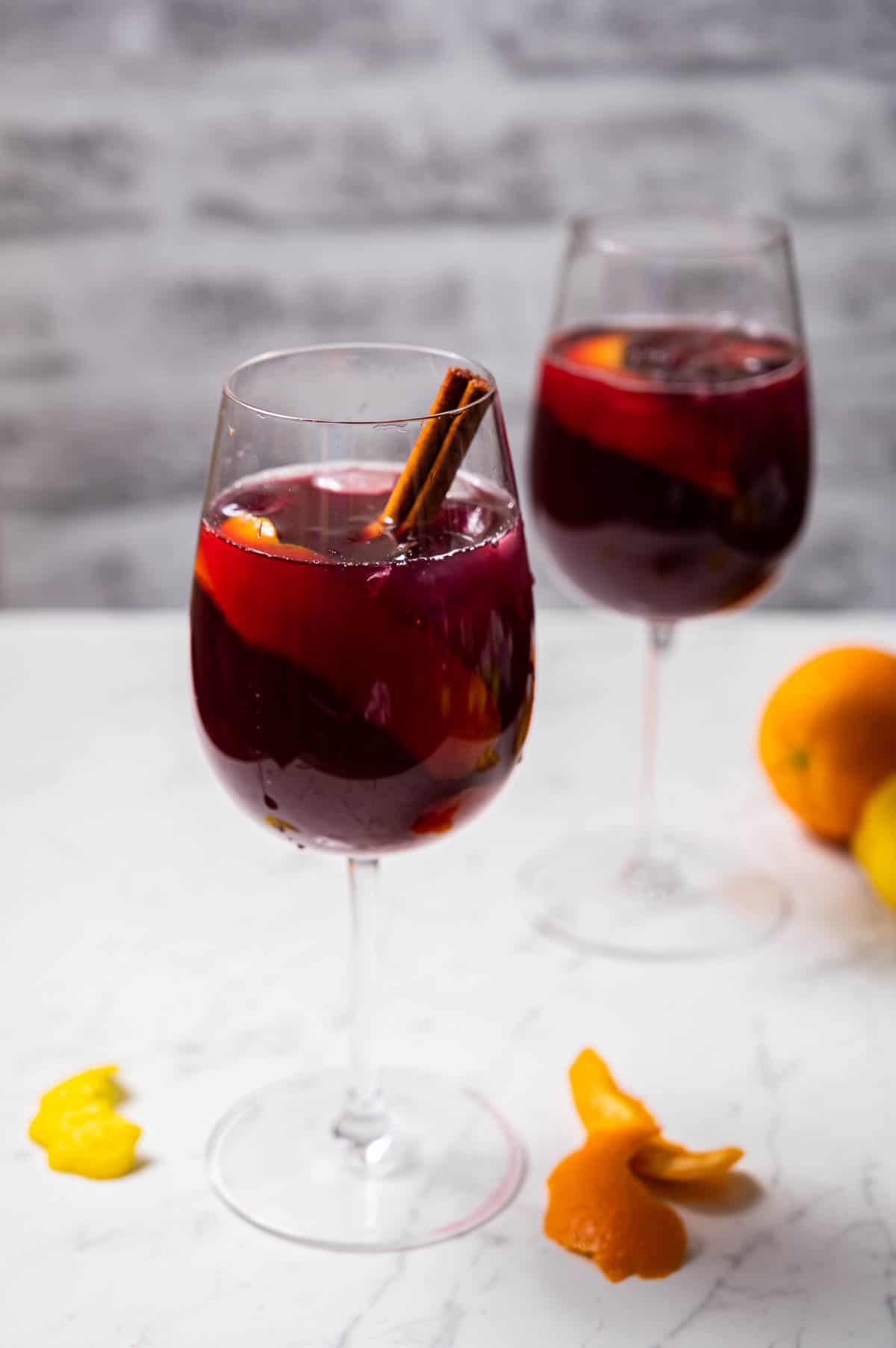 Two wine glasses of sangria garnished with cinnamon sticks and citrus