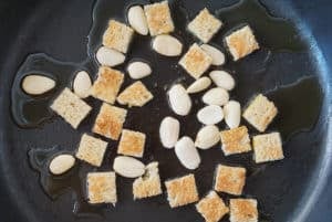 Cubed bread and almonds in a frying pan with olive oil