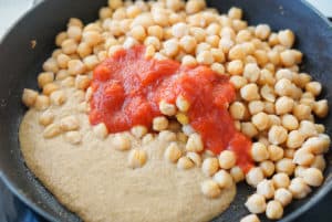 A frying pan with almond, garlic and bread paste next to garbanzo beans and tomato sauce