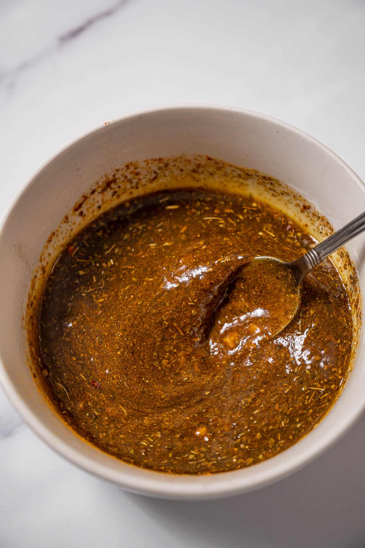 Ras el hanout marinade in a white bowl with a metal spoon