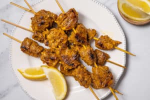 Spanish pork skewers on a white plate with lemon wedges.