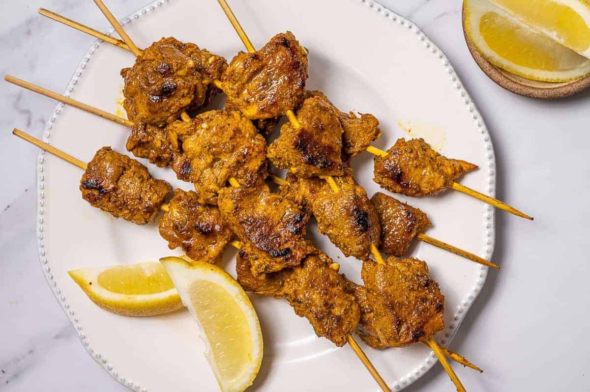 Spanish pork skewers on a white plate with lemon wedges.