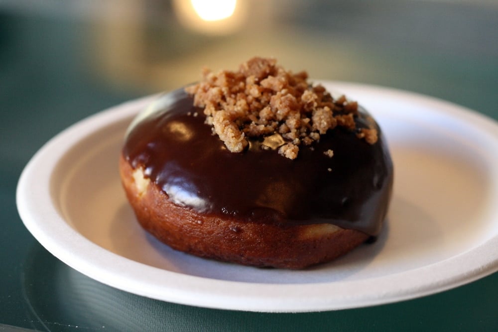 Close-up of a chocolate-covered doughnut with brown crumble on top, on a white plate.