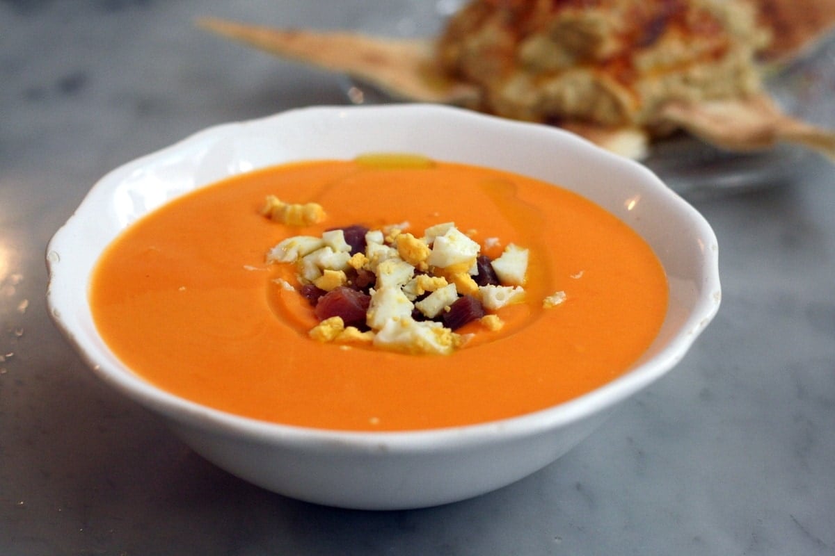 chillled tomato soup in a white bowl topped with hard boiled egg and ham