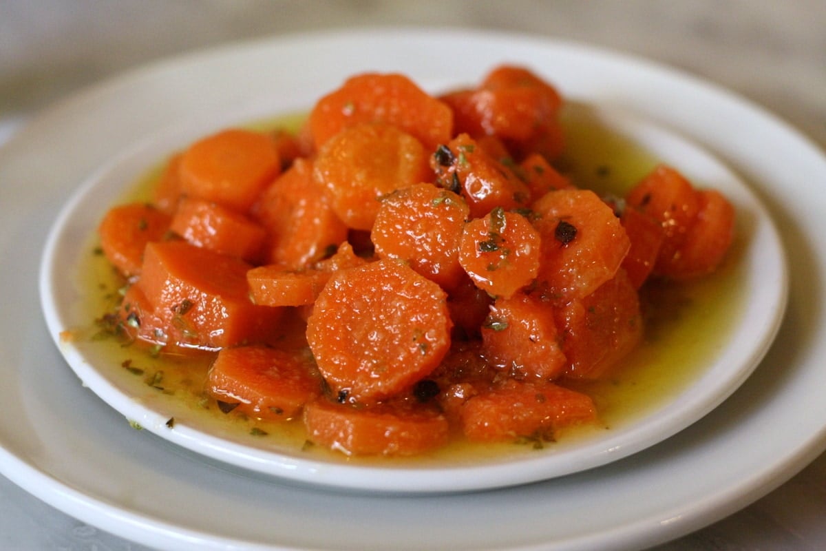 Close-up of a plate of sliced carrots marinated in olive oil and herbs.