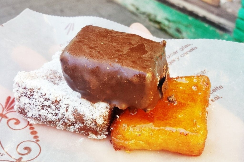 Three rectangular pieces of torrija with powdered sugar, honey syrup, and chocolate coating.