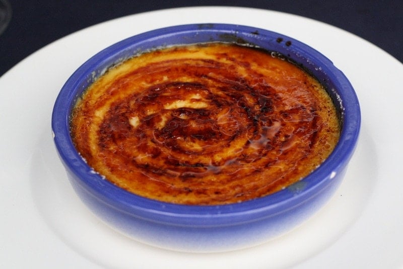 A round blue dish of crema catalana, a custard dessert with a burnt sugar top.