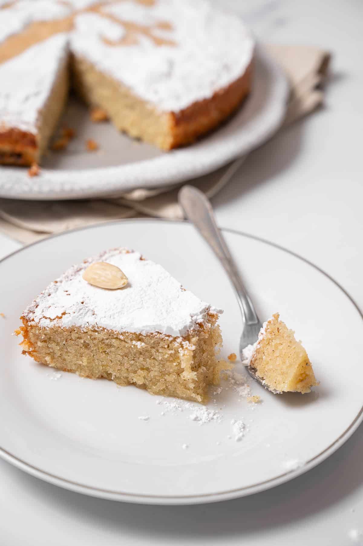 Spanish almond cake slice on a white plate with a bite taken on a fork.