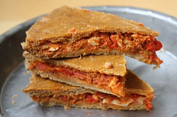 A stack of three slices of Spanish empanada: chopped tuna filling between two crusts.