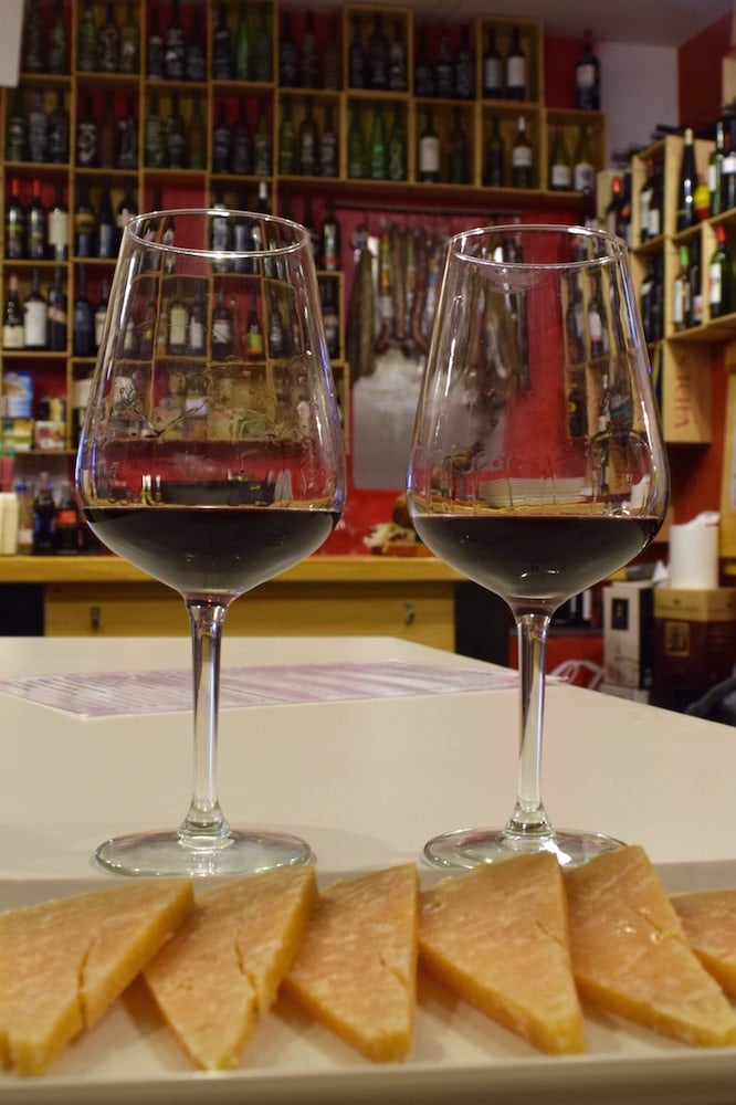 Close-up of two glasses of red wine and a plate of sliced cheese.