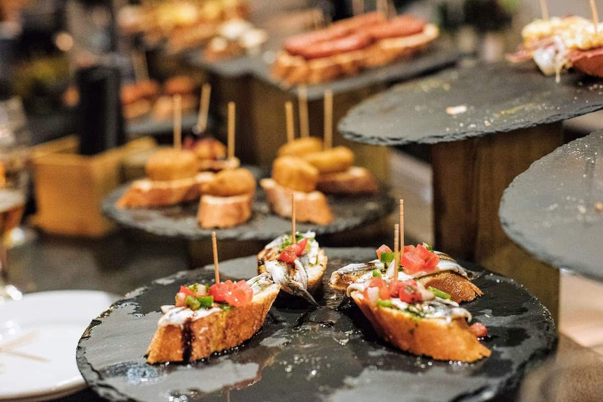 Tray of small slices of bread with anchovies and chopped vegetables held on top with toothpicks.