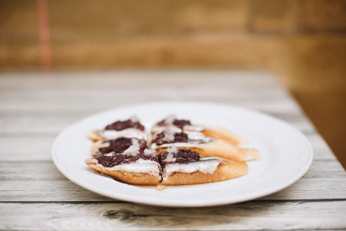 Three small slices of artisanal bread topped with white anchovies and black olive tapenade.