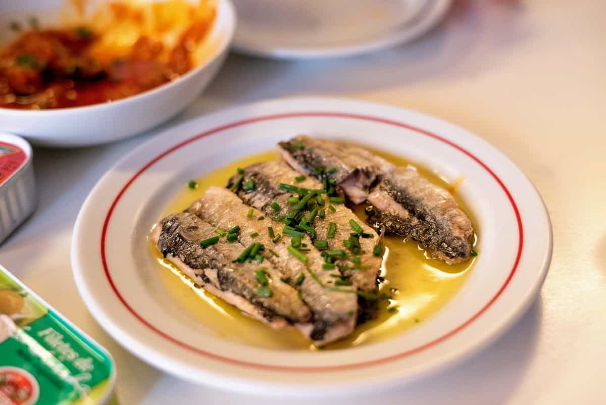 A plate of preserved fish slices in olive oil, topped with herbs.