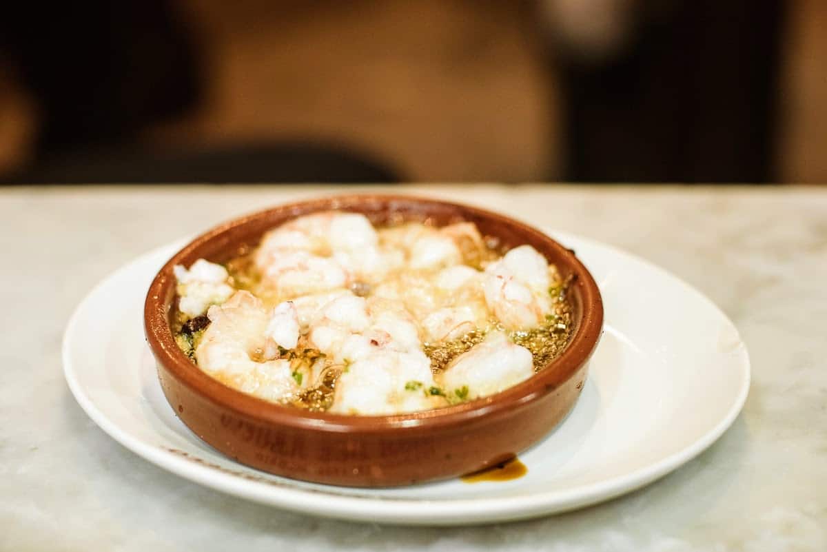 Small clay dish of shrimp in a garlic-olive oil sauce.