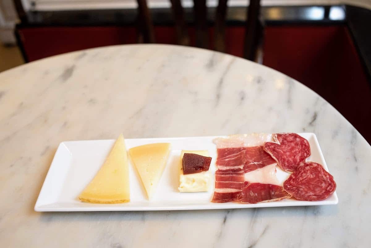 A few slices of Spanish cheese and cured meats on a small tapas platter.