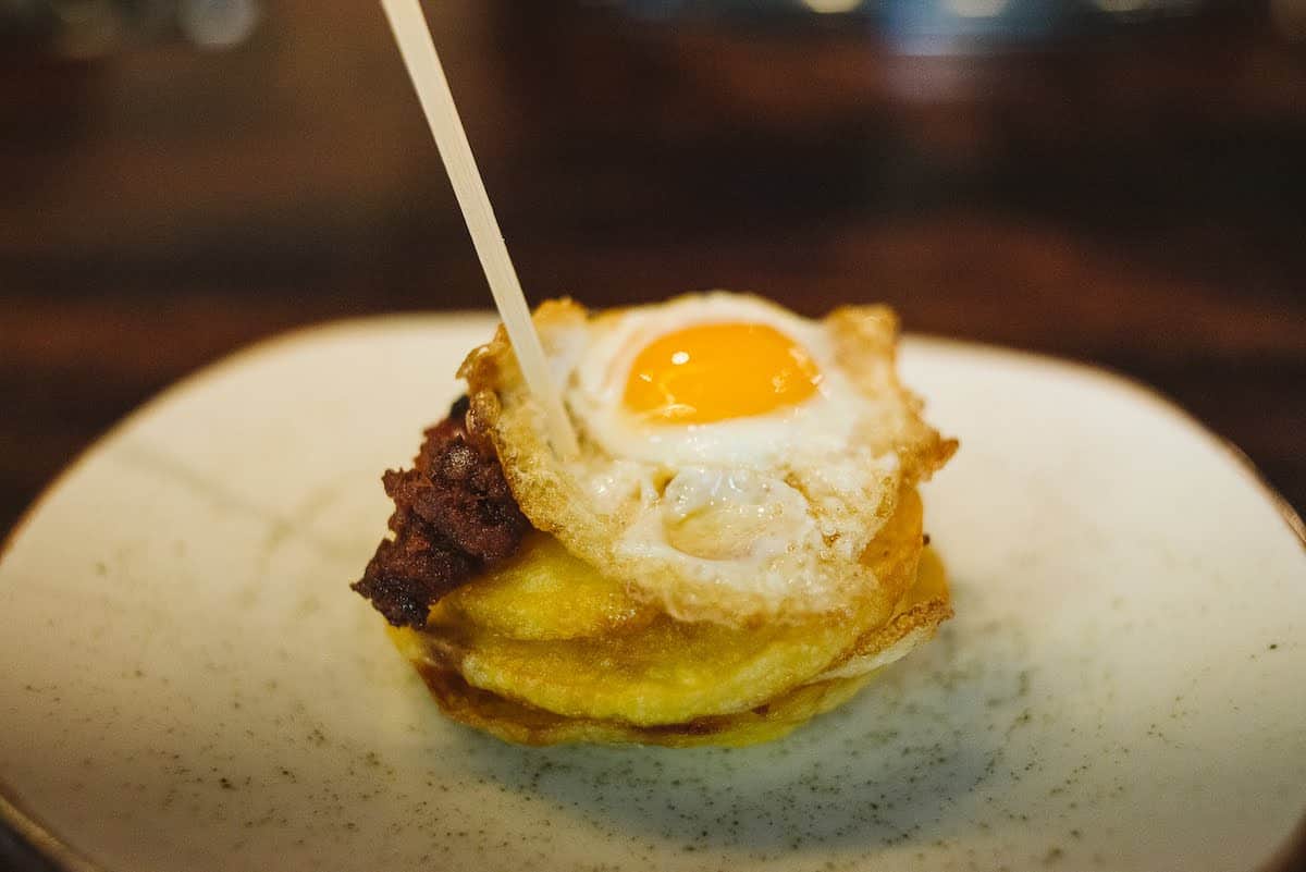 Stack of fried potato rounds topped with an egg and garnished with crumbled chorizo.