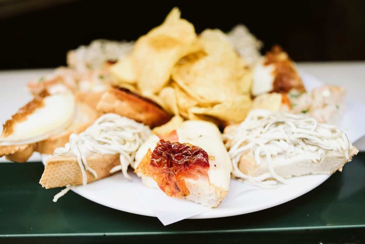 Platter of toasted bread slices with various toppings, with a pile of potato chips in the middle