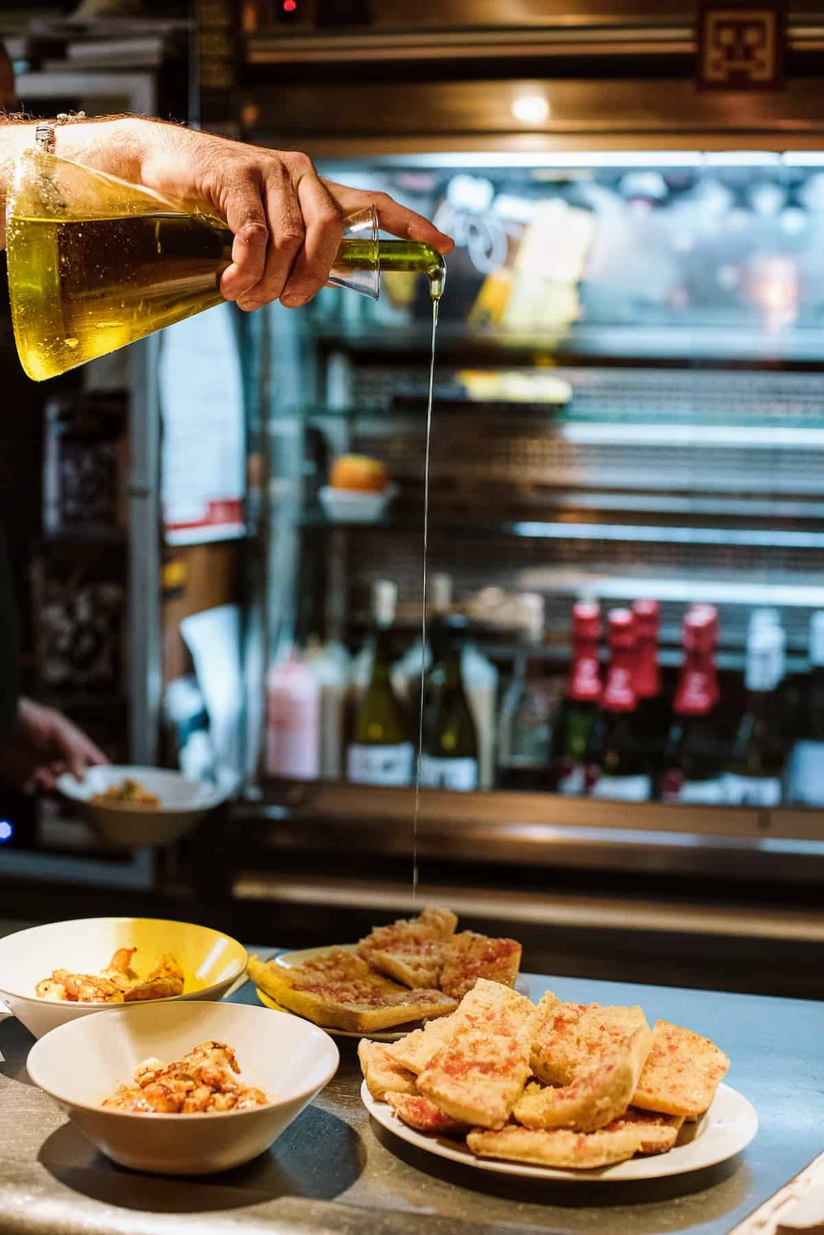 A person's hand pouring olive oil over a plate of toasted bread with tomato.