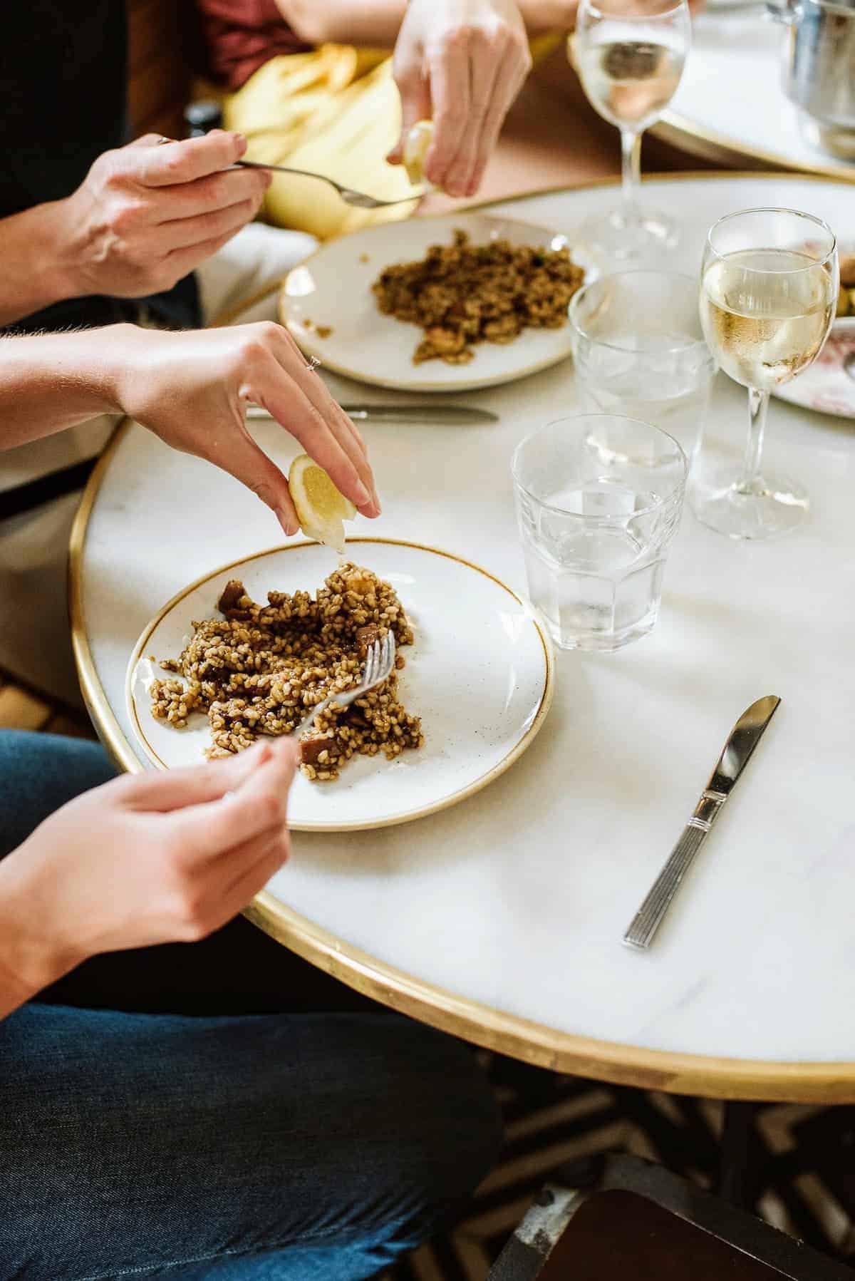 Person's hand squeezing a lemon wedge over a plate of rice with brown sauce.