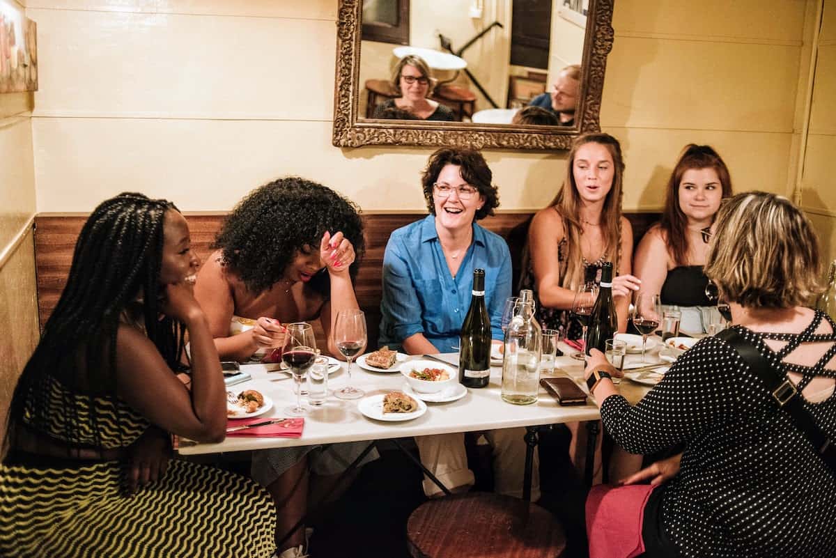 A group of people seated around a restaurant table, eating shared plates and talking.