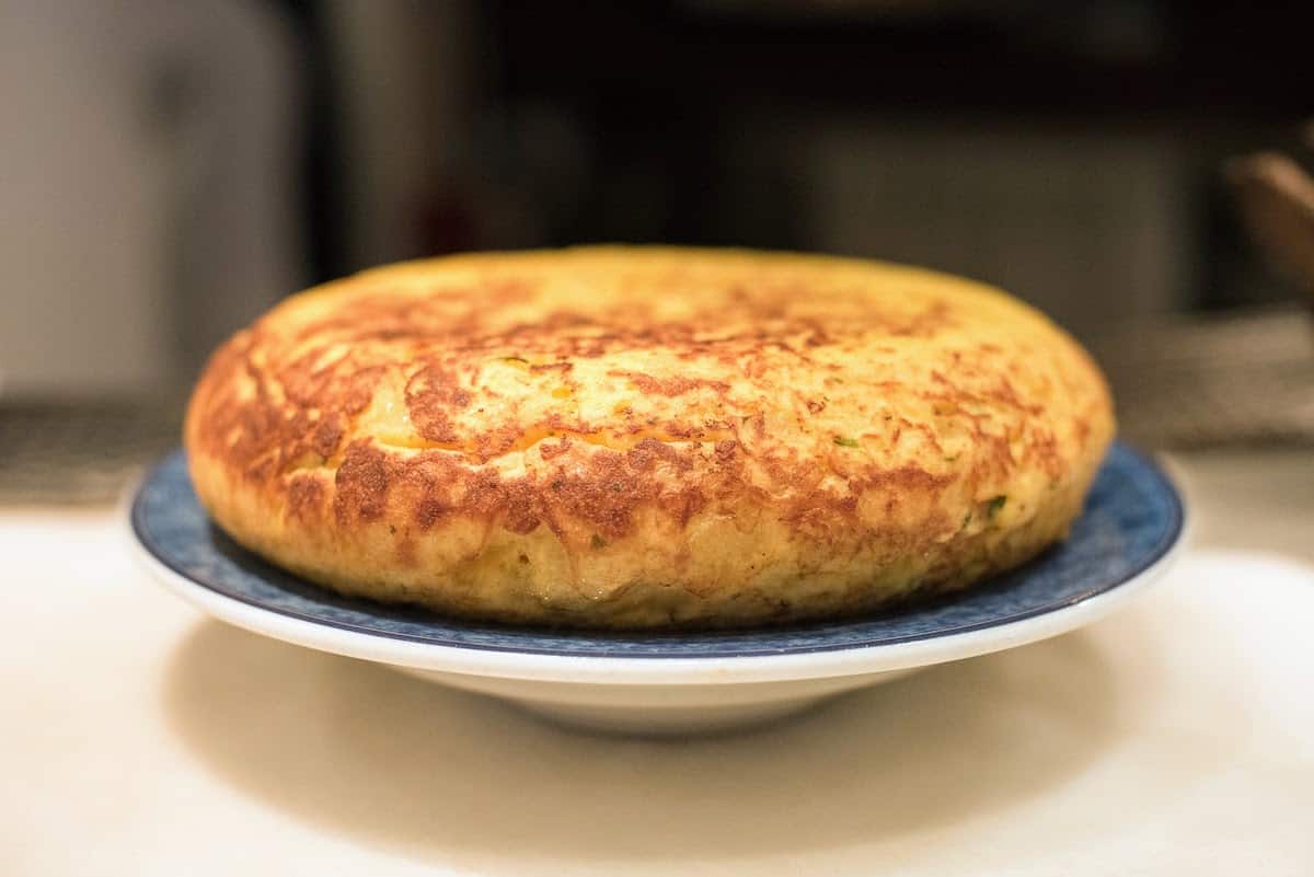 A golden-brown tortilla de patatas (Spanish potato omelet) on a blue plate.