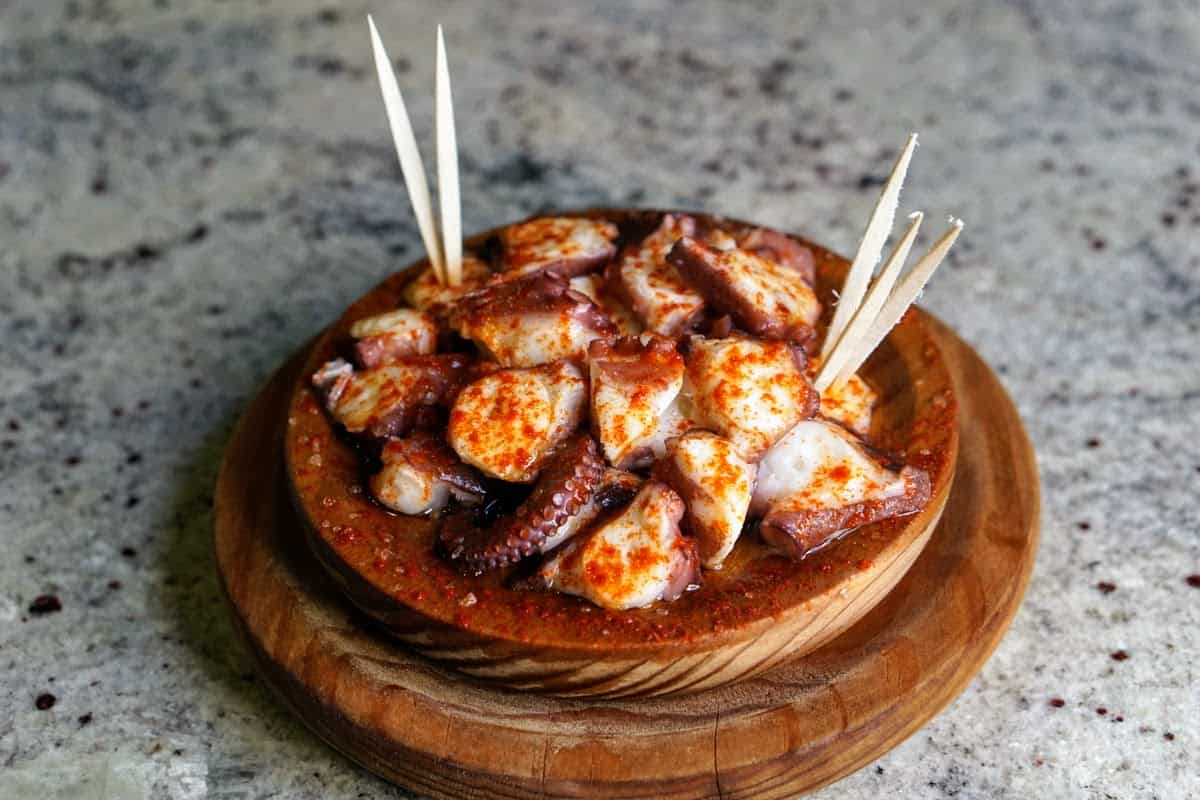 Slices of boiled octopus covered in paprika and served in a wooden dish with toothpicks.