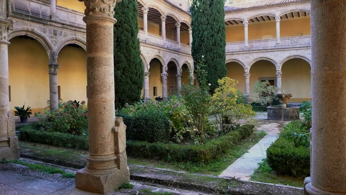 Interior courtyard of an old monastery full of green plants and surrounded by stone archways.