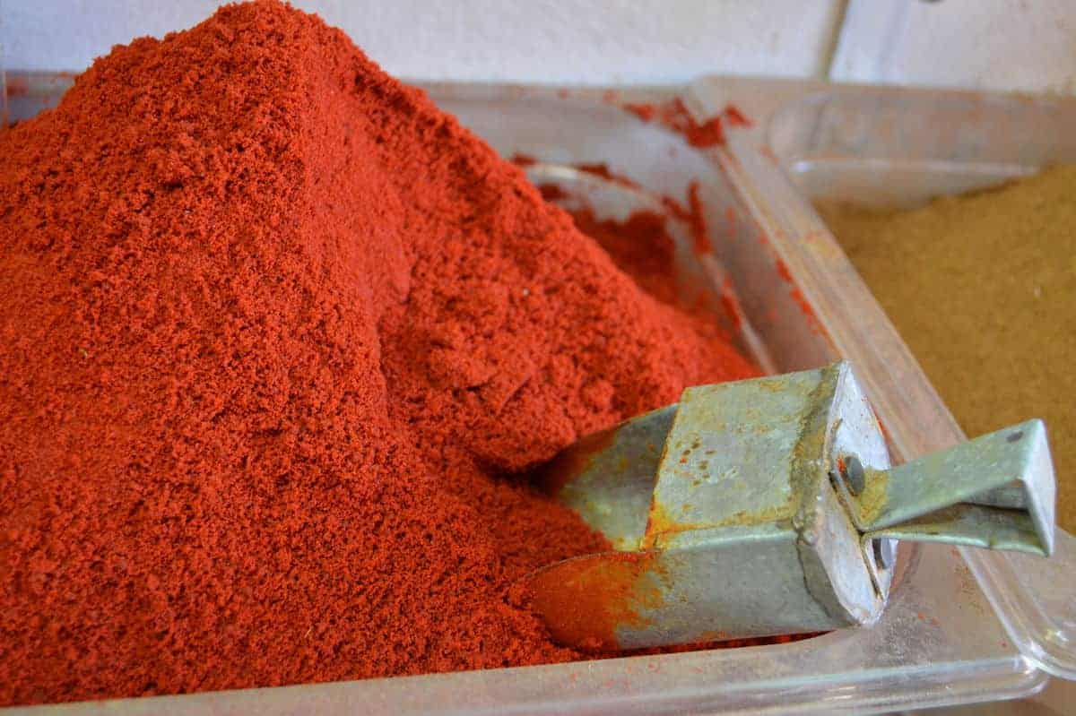 Close-up of a mound of bright red smoked paprika sold in bulk, with a metal scoop.