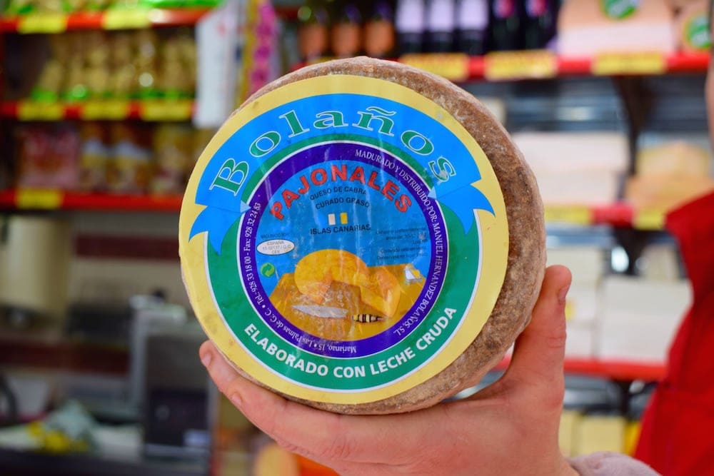 Close-up of someone holding a wheel of cheese with a colorful label reading "Bolaños Pajonales."