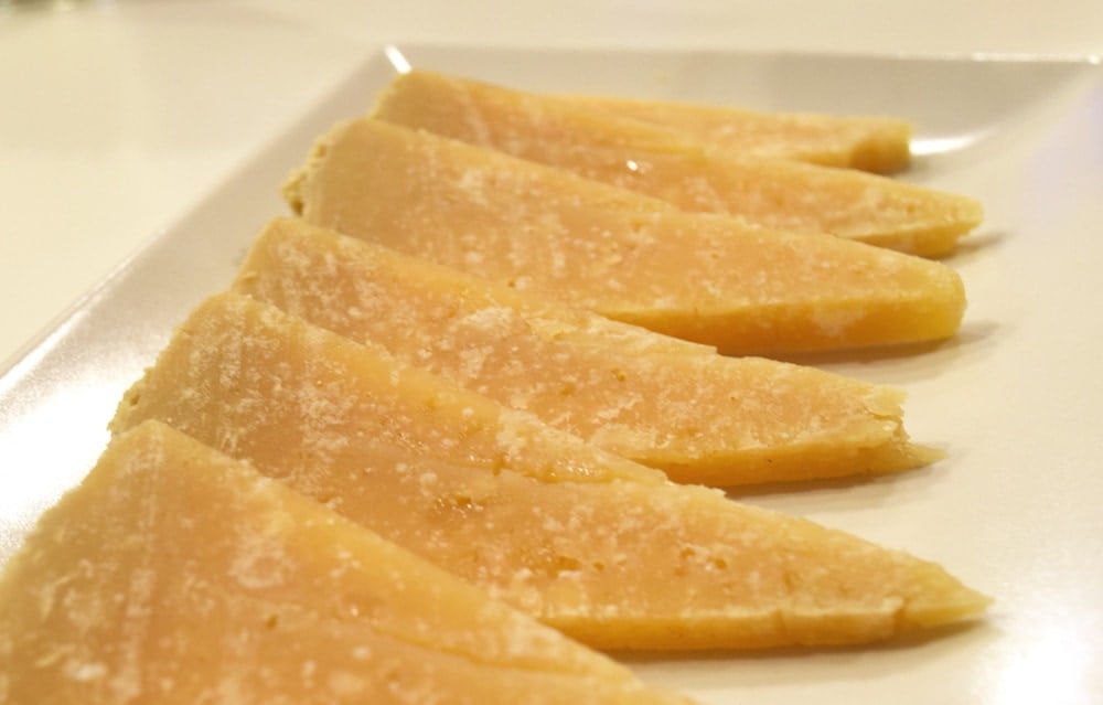 Close-up of six triangular slices of cured Manchego cheese on a white plate.