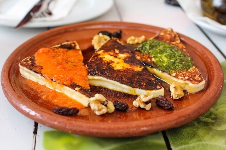 A clay plate with three triangles of grilled cheese topped with red and green sauces.