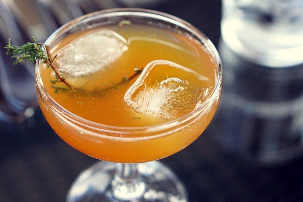 Close-up of an orange cocktail with ice and a sprig of thyme.