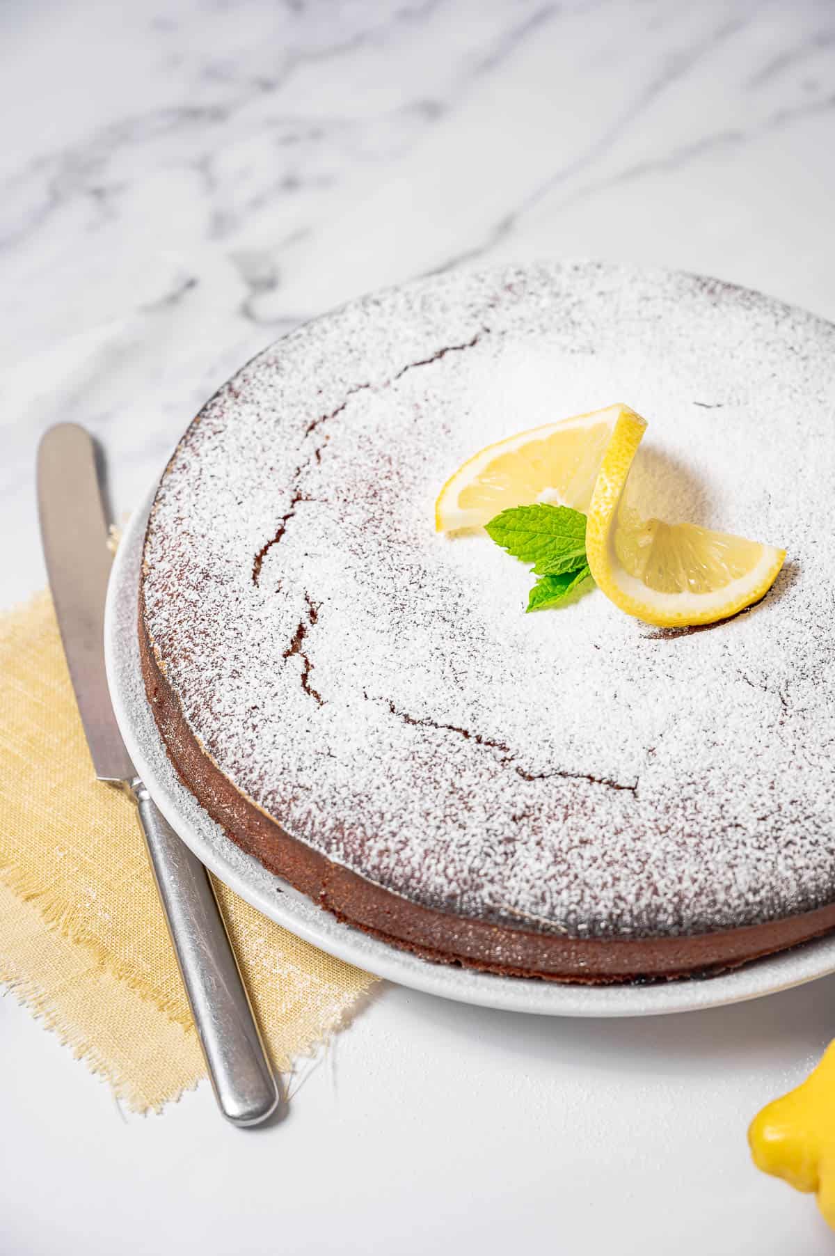 Lemon olive oil cake with almonds on a white cake dish topped with sliced lemon