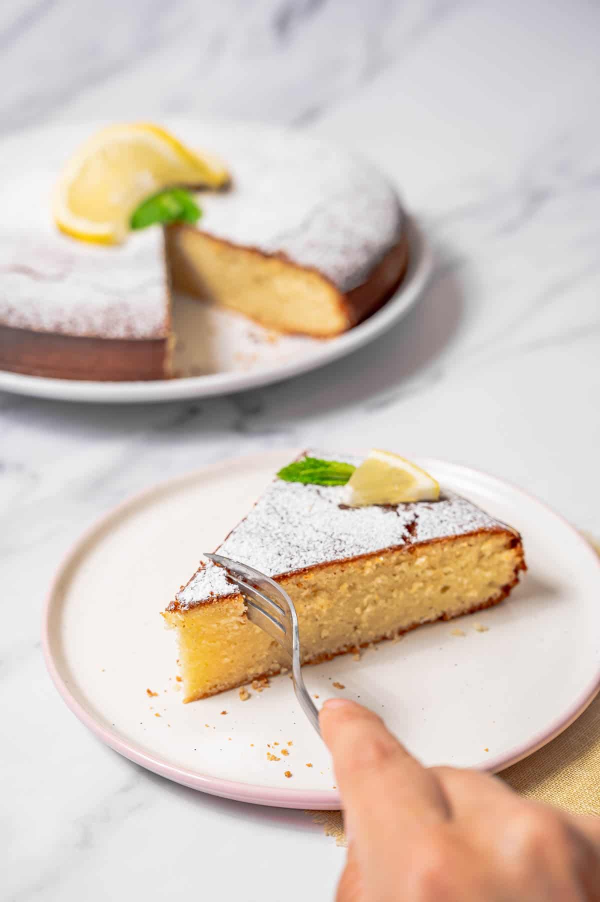 Cutting into a slice of lemon olive oil cake on a white plate