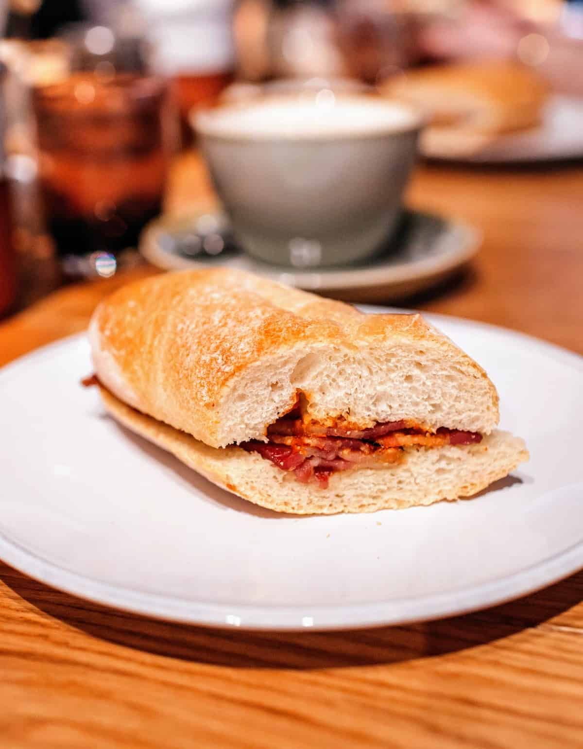 Sandwich made with baguette style bread and filled with cured meat on a white plate