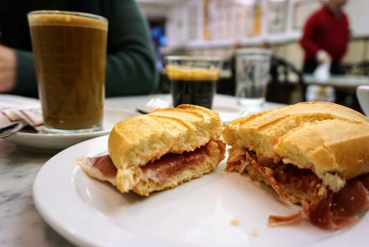 Toasted cured ham sandwich cut in half beside a clear glass of coffee
