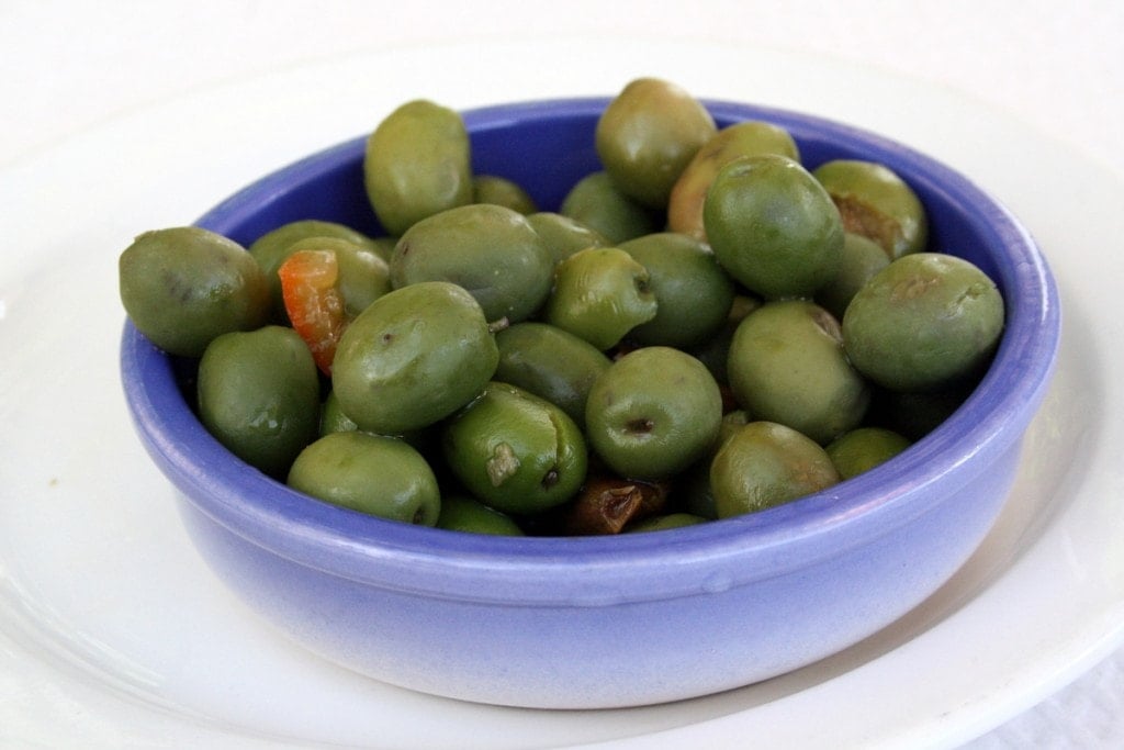 A small blue dish of dark green olives on a white surface.