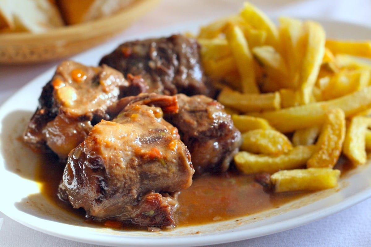 A plate of stewed bull tail in a brown sauce with a pile of French fries.