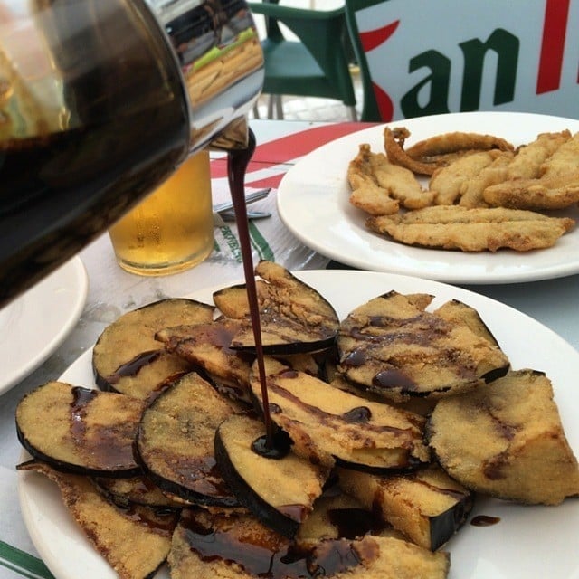 A plate of fried eggplant slices with dark brown molasses being drizzled over them. 