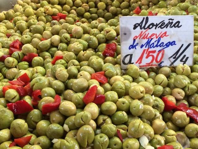 Close-up of green olives mixed with red pepper, with a sign showing their price by weight.