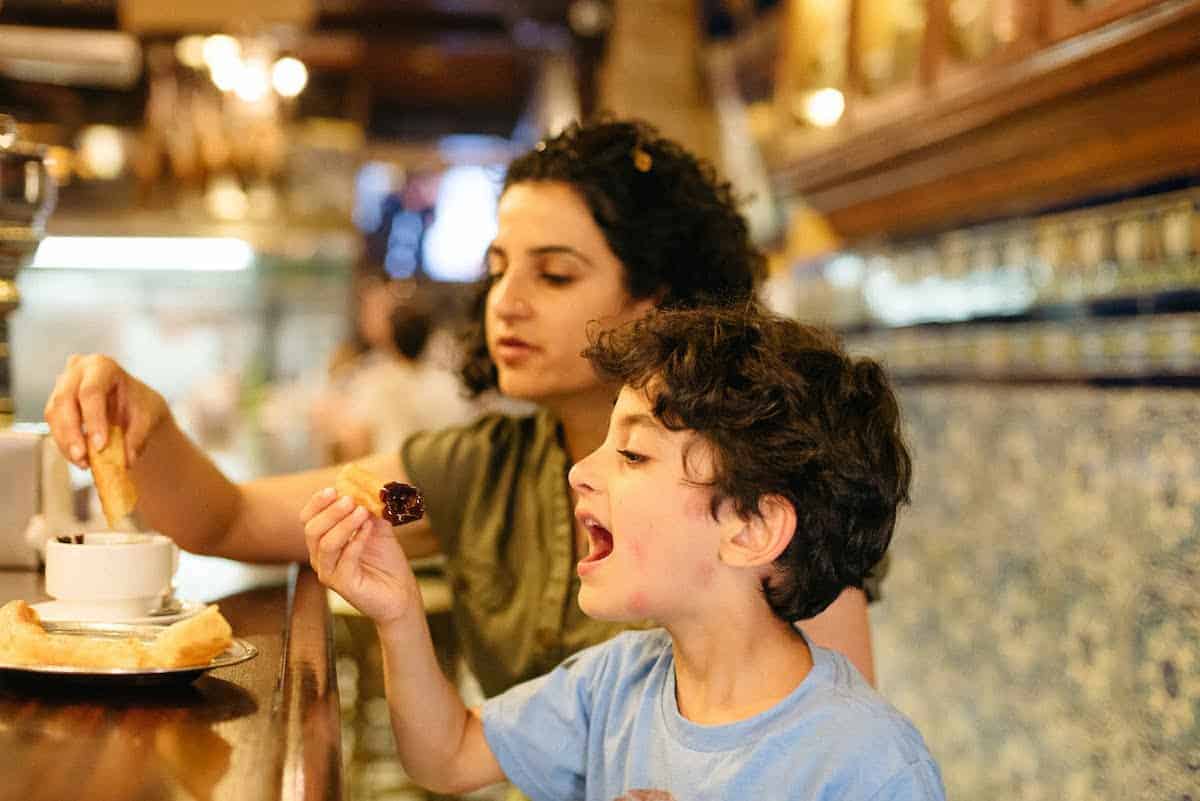 Mother and child sitting at a wooden bar eating churros and chocolate