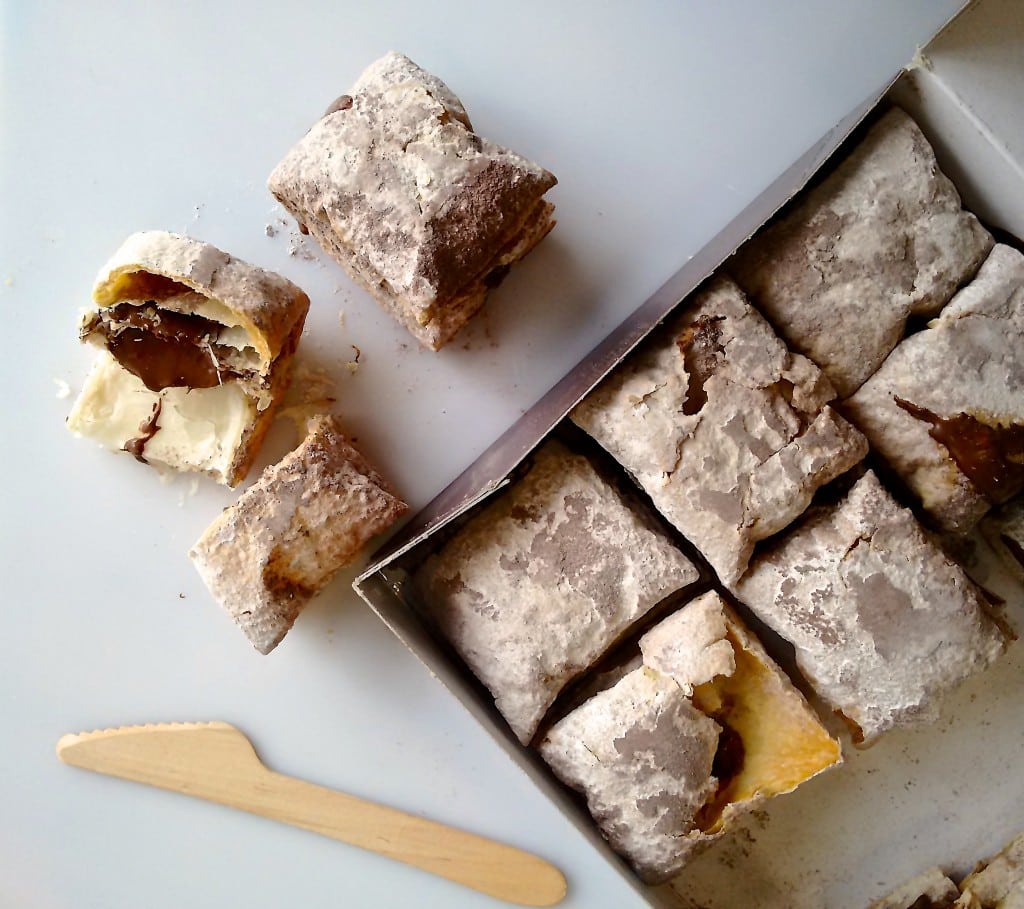 A box of Miguelitos—Spanish puff pastry squares filled with chocolate—with one cut in half.