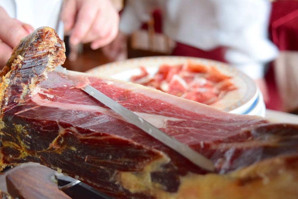 Close-up of a leg of Spanish ham being sliced with a long knife.