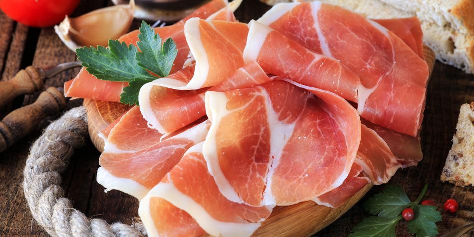 Close-up of sliced jamón serrano garnished with a sprig of green herbs.