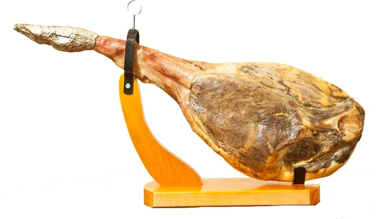 A whole leg of Spanish ham in a wooden carving stand, on a white background.
